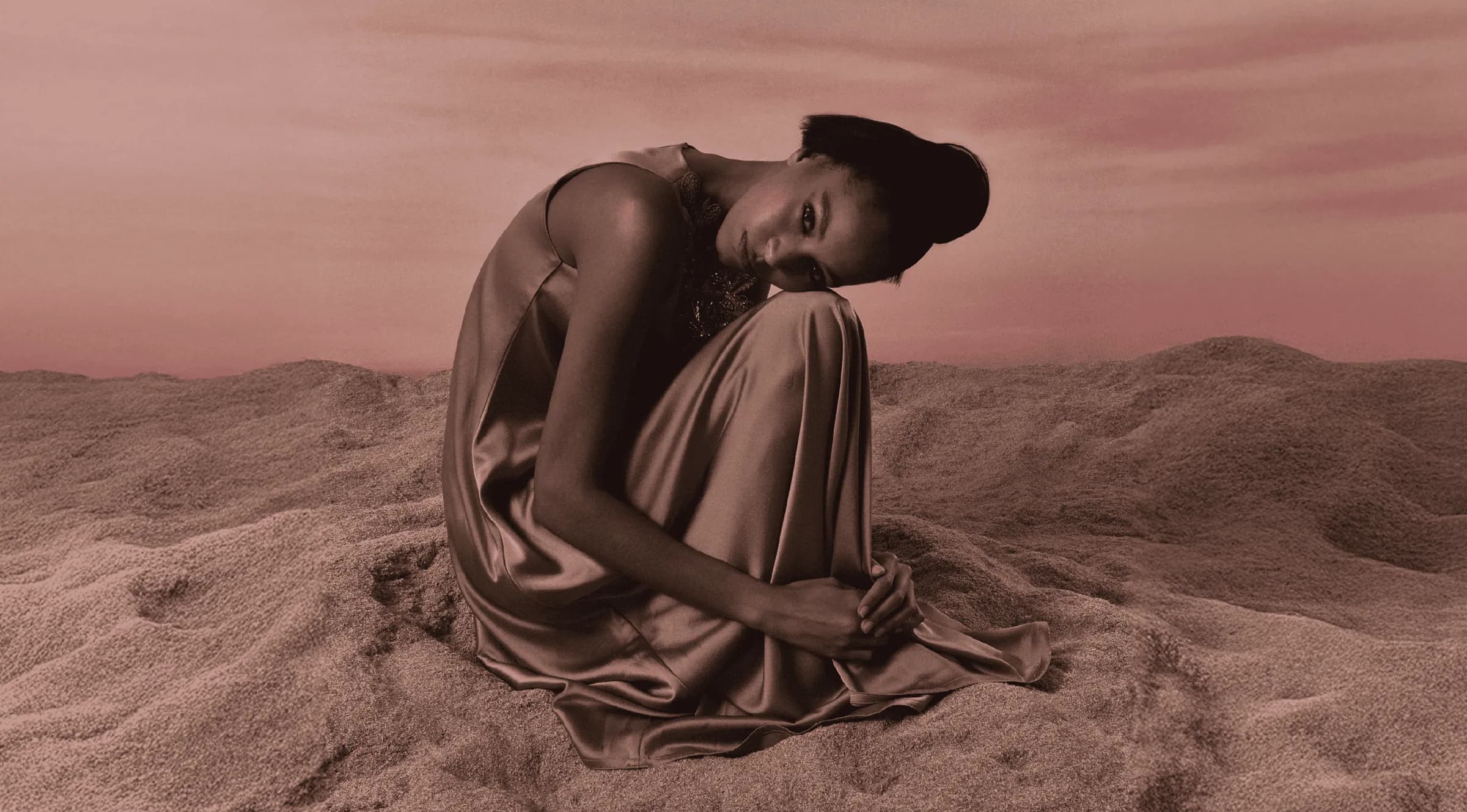 Model in flowing fabric seated in desert dunes, cinematic shot